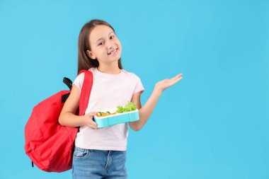 Sırt çantası ve mavi arka planda beslenme çantası olan mutlu küçük kız.