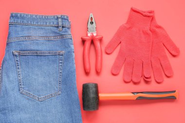Kırmızı arka planda aletler, eldivenler ve kot pantolon. İşçi Bayramı kutlamaları