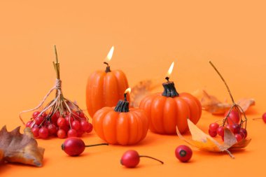 Balkabağı şeklinde yanan mumlarla ve turuncu arka planda sonbahar yapraklarıyla güzel bir kompozisyon.