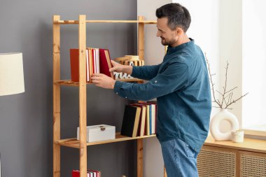 Yakışıklı adam evdeki raftan kitap alıyor.