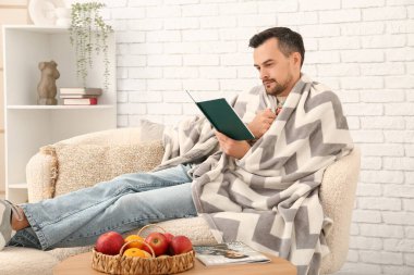 Oturma odasında ekose kitap okuyan yakışıklı bir adam.