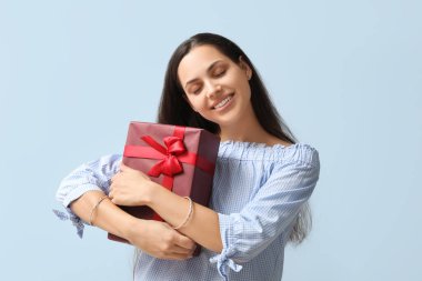 Mavi arka planda hediye kutusu olan mutlu genç bir kadın.