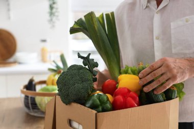 Mutfakta karton kutu taze sebzeli olgun bir adam, yakın plan.