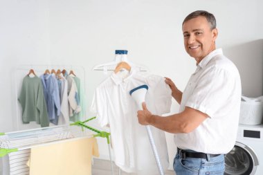 Olgun bir adam evde beyaz gömlek buharlaştırıyor.