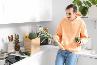 Mutfaktaki tezgahta elinde bir torba taze sebze olan genç adam.