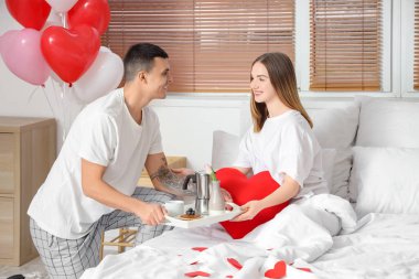 Genç adam sevgililer gününde güzel karısına yatakta kahvaltı getiriyor.