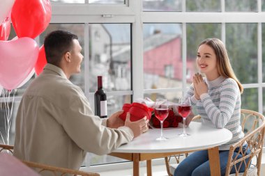 Evde Sevgililer Günü 'nü kutlamak için ellerinde şarap ve hediye kutusuyla güzel bir çift.