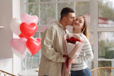 Bir buket gülle öpüşen ve evde Sevgililer Günü 'nü kutlayan güzel bir çift.