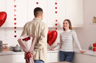 Genç adam sevgilisini evinde Sevgililer Günü için bir buket gülle selamlıyor.