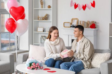 Hediye kutusu, çiçek buketi ve evde Sevgililer Günü 'nü kutlayan kalp şeklinde balonları olan genç ve güzel bir çift.