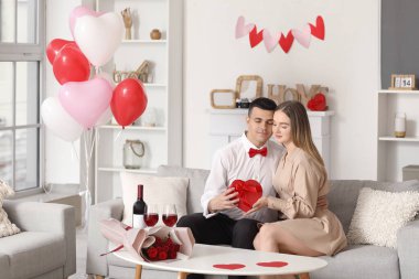 Sevgililer Günü 'nü evde kutlayan bir buket çiçek ve şarap kadehi olan güzel bir çift.