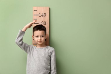 Yeşil arka planda boyunu ölçen sevimli küçük bir çocuk.