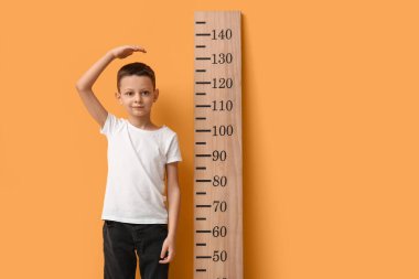 Sarı arka planda boyunu ölçen sevimli küçük bir çocuk.