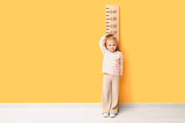 Sarı duvarın yanında boyunu ölçen sevimli küçük bir kız.