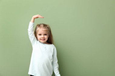 Yeşil arka planda boyunu ölçen sevimli küçük bir kız.