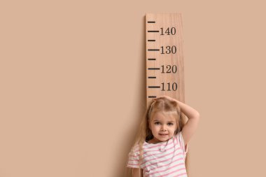 Bej arkaplanla boy ölçüşen sevimli küçük kız.