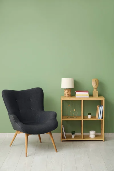 Shelving unit with books, decor and armchair near green wall in room