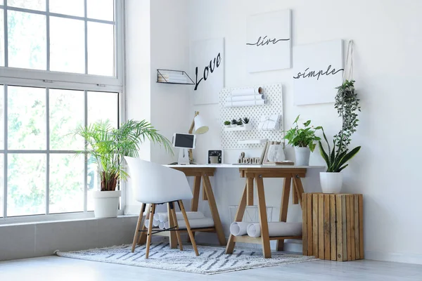 Interior of light office with workplace, pegboard and houseplants