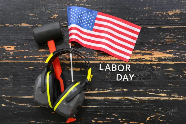 Earmuffs, rubber mallet, USA flag and text LABOR DAY on black wooden background