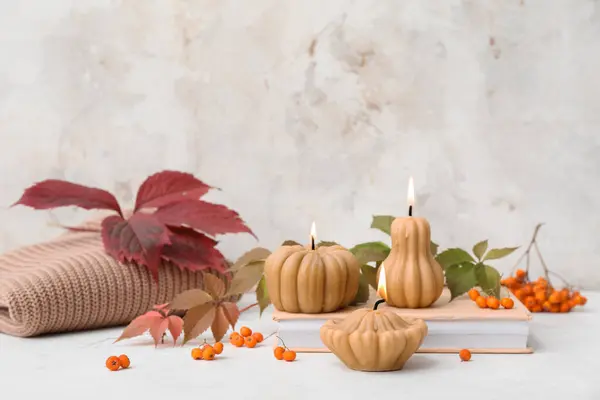 Beautiful autumn composition with burning candles in shape of pumpkin and book on white background
