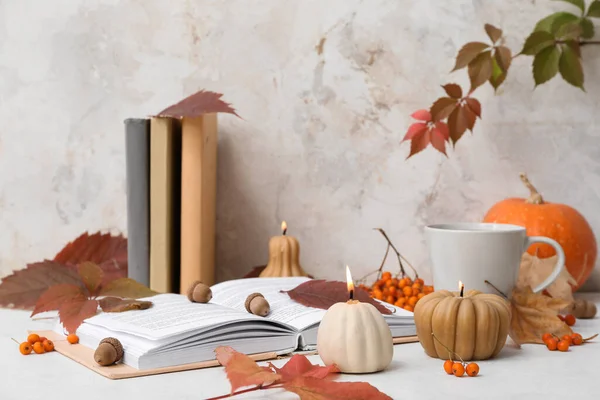 Beautiful autumn composition with burning candles in shape of pumpkin and book on table near beige wall