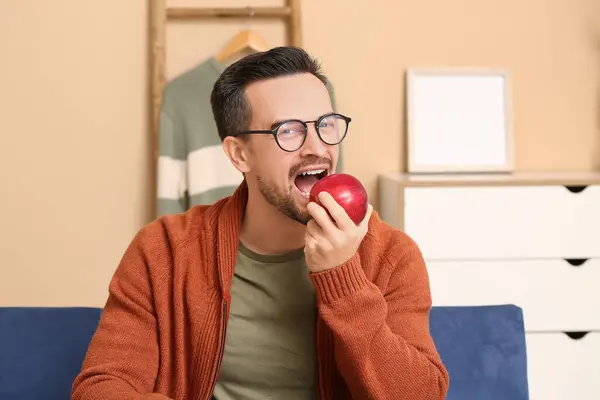 Handsome man eating apple in living room, closeup