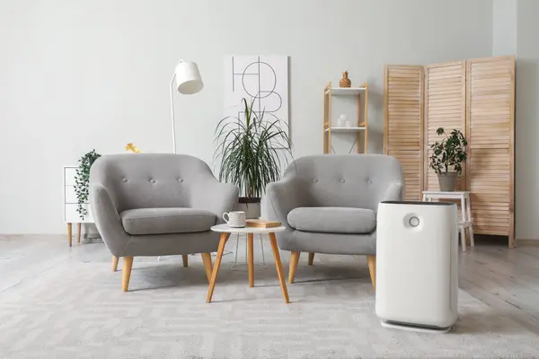 Interior of living room with air purifier, grey armchairs and houseplants