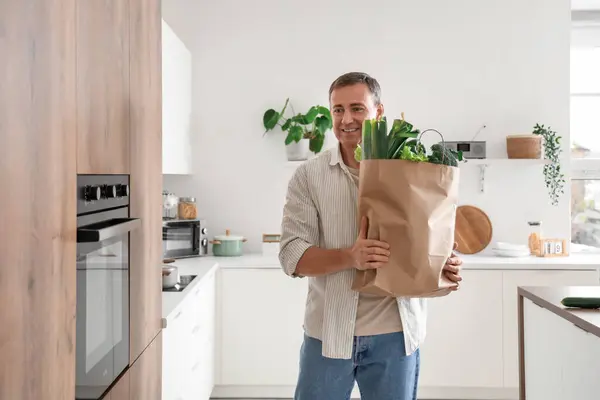 Mature man with paper bag of fresh vegetables in kitchen