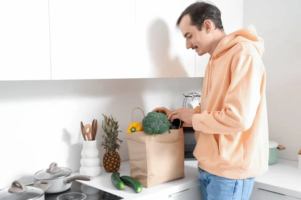 Young man with paper bag of fresh vegetables on counter in kitchen