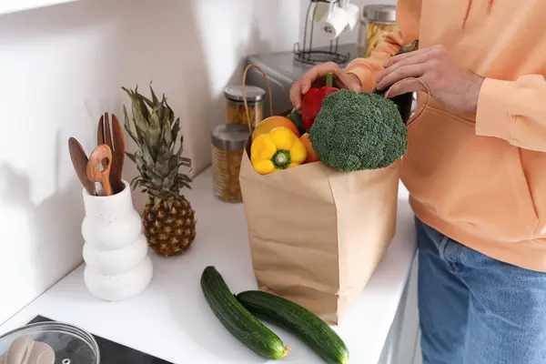 Young man with paper bag of fresh vegetables on counter in kitchen, closeup