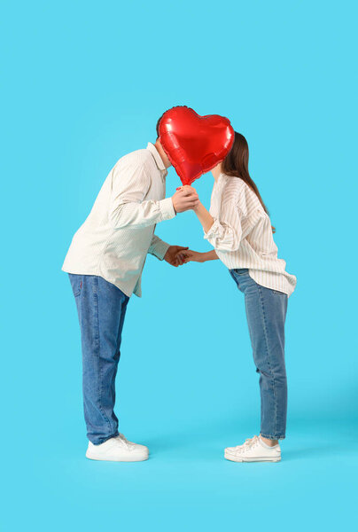 Lovely couple covering face with heart-shaped balloon on blue background. Valentine's Day celebration