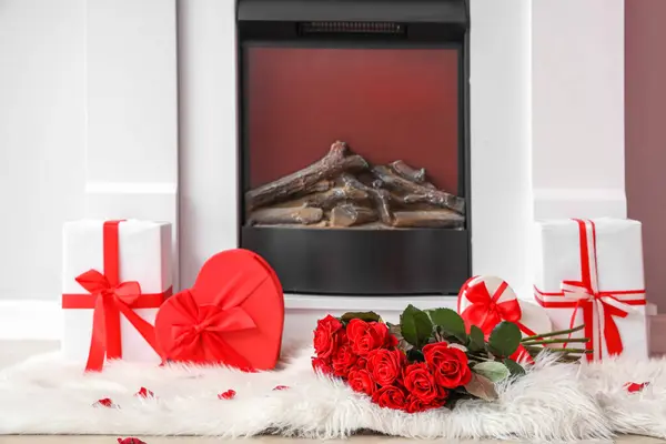 Bouquet of beautiful roses and gift boxes on fur rug near fireplace. Valentine\'s Day celebration