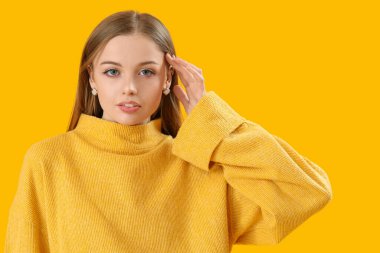 Fashionable young woman in knitted sweater on yellow background