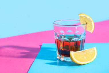 Bir bardak limon dilimli rom ve renkli arkaplanda buz.