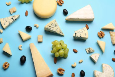 Farklı çeşitlerde lezzetli peynir, fındık ve üzümler mavi arka planda.