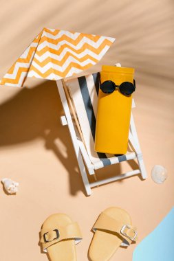 Sahilde suya yakın minyatür şezlonga, şemsiyeye ve güneş kremine sahip yaratıcı kompozisyon
