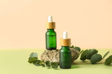 Okaliptüs dalları ve yeşil masa üzerinde taş olan kozmetik yağları.