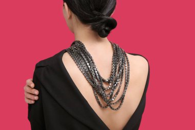 Kırmızı duvarın yanında kocaman bir kolye takan güzel bir kadın.