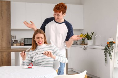 Genç adam, mutsuz kız arkadaşına mutfakta evlenme teklif ediyor.