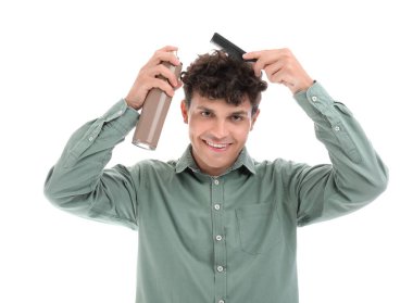 Kıvırcık saçlarına beyaz arka plana saç spreyi sıkan yakışıklı bir genç.