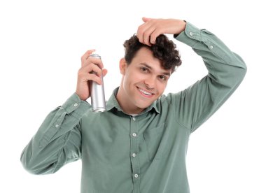 Kıvırcık saçlarına beyaz arka plana saç spreyi sıkan yakışıklı bir genç.