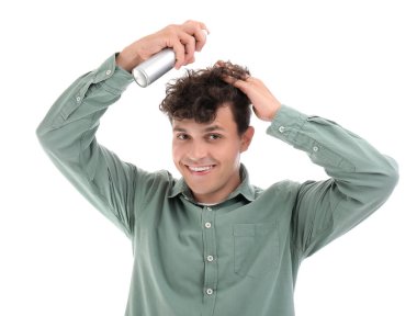 Kıvırcık saçlarına beyaz arka plana saç spreyi sıkan yakışıklı bir genç.