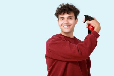 Kıvırcık saçlarına mavi arka planda saç spreyi sıkan yakışıklı bir genç.