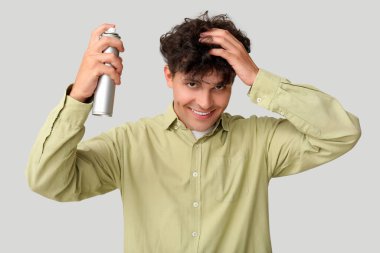 Kıvırcık saçlarına gri arka planda saç spreyi sıkan yakışıklı bir genç.