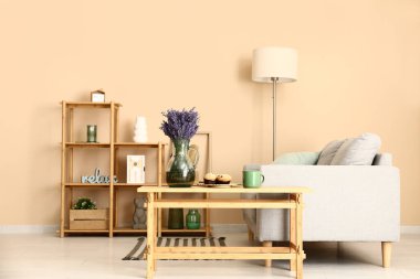 Şık oturma odasının içinde raf ünitesi, kanepe, lamba, masa ve güzel lavanta çiçekleri