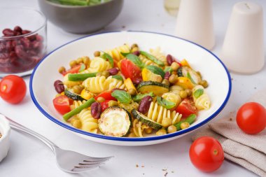 Bir kase domatesli makarna salatası ve beyaz arka planda fesleğen.