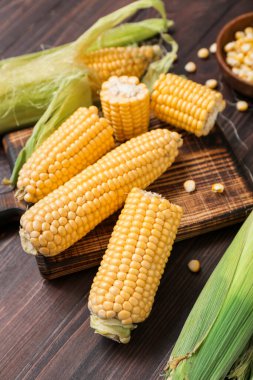 Koyu ahşap masada taze mısır koçanları, yakın plan.