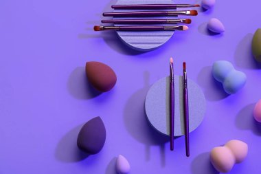 Dekoratif podyumlar makyaj fırçaları ve eflatun arka planda süngerler