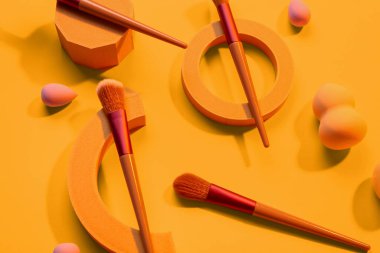 Sarı arka planda makyaj fırçası ve süngeri olan dekoratif podyumlar