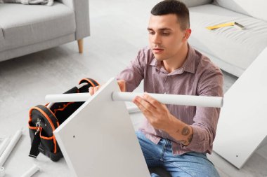 Genç adam evde mobilya montajı yapıyor.